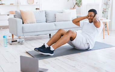 Home Training. Sporty African American Man Exercising Doing Sit-Ups Abs Exercise At Laptop Computer Indoors. Online Sport Workout, Morning Physical Training Exercises Concept