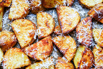 Pieces of potatoes are baked on a baking sheet, sprinkled with cheese. Background with rustic...