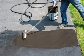 Spreading asphalt driveway sealer on a dampened driveway