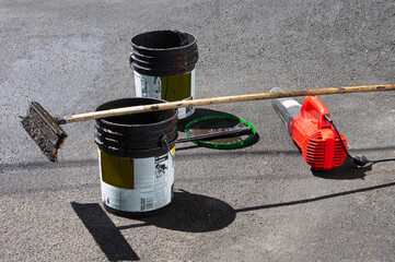 A wiper tool for spreading, a blower for cleaning debris, and buckets of asphalt are needed to reseal driveway