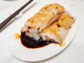 Har cheung fun or shrimp rice noodle roll served with a delicious dark sauce served on a oval plate isolated on a marble background.
