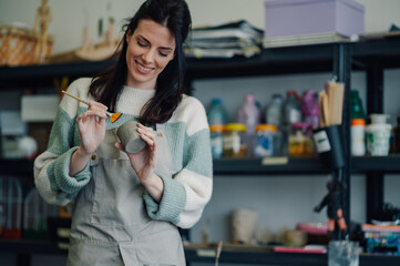Ceramist painting a small pot in her workshop