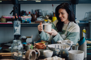 Ceramist woman holding a clay pot in her workshop