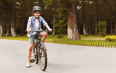 Urban Lifestyle. Smiling curly boy standing on a bicycle in park and posing, looking at camera,...