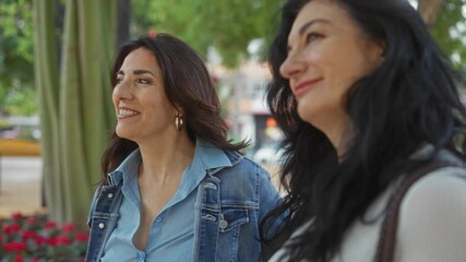 Mature women friends enjoying a pleasant conversation in an urban park, showcasing genuine happiness and togetherness amidst a vibrant city backdrop.