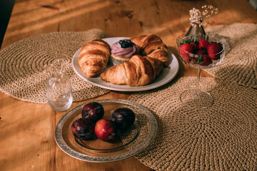 Still life with croissants, cupcakes, plums and strawberries on a wooden vintage table. Elegant...