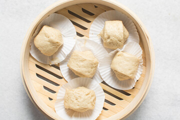 Overhead view of steamed bun dough in a steamer basket, top view of mantou dough in a bamboo steamer, process of making steamed milk buns