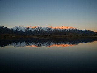 Fototapeta premium Lake Heron idyllic calm serene golden hour orange mountain peak winter sunset mirror reflection, Southern Alps landscape, Ashburton Lakes New Zealand