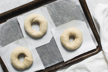 Overhead view of proofed bagel dough, top view of raw homemade bagels on parchment lined baking...