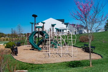 Outdoor playground with vines and slides surrounded by a green lawn with benches for parents.