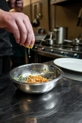 A chef adds fresh lemon juice to a stainless steel bowl containing chopped vegetables and herbs, showcasing the preparation of a vibrant ingredient mix in a professional kitchen.