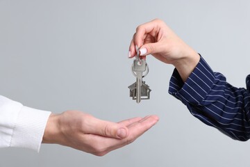Real estate agent giving house key to new owner on gray background, closeup