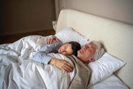Calm mature couple of husband and wife cuddling in bed, enjoying restful sleep in intimate bedroom. Bond peaceful rest, gentle embrace hug of husband, tranquil healthy sleep, love in simplicity 