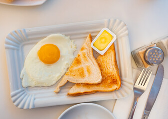 Appetizing fried egg on plate with toasted toast and portioned butter on a served table in a cafeteria