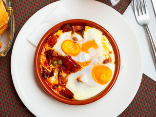 Delicious dish of Spanish cuisine is broken roasted eggs with chistorra, cut into pieces, and green...