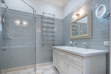 A clean and modern bathroom with light grey tiled walls, a stylish dressing table with a sink and a...