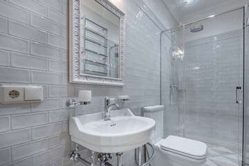 The modern bathroom is decorated in a minimalist style with white tiles on the walls and a glass shower.  Stylish and elegant interior details.