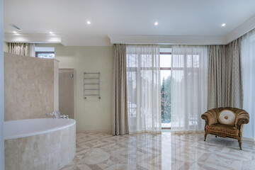 A spacious bathroom with a large bathtub and a stylish armchair. The natural lighting pouring...
