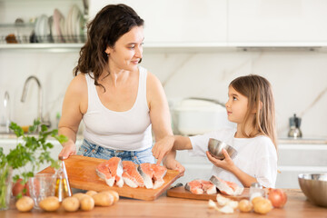 Happy mother and her daughter preparing pieces of salmon to bake in the kitchen