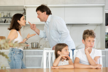 Fototapeta premium Brother and sister sitting at table in kitchen during conflict between their parents