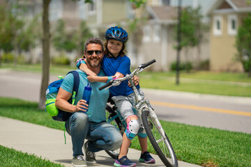 Obraz premium Happy fathers day. Father teaching son cycling on bike. Happy loving family. Father and son hugging. Father support and helping son. Fathers day concept. Friendly family. Father and son friends.