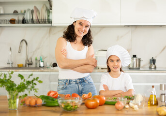 Mother with little girl in white cooking hats posing in kitchen, cooking class for small child.