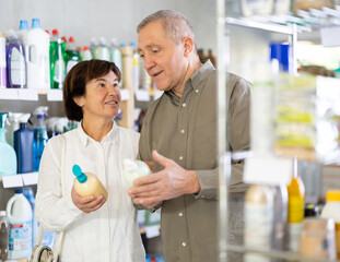 Obraz premium Elderly husband and wife choose a moisturizing liquid hand soap in the supermarket. Pensioners in a household store buy cream soap with a natural composition