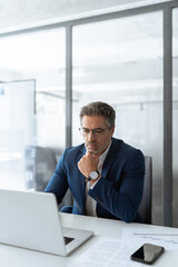 Focused senior businessman entrepreneur sitting at desk working on financial project, looking...