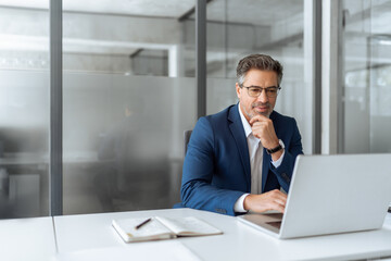 Focused senior businessman entrepreneur sitting at desk working on financial project, looking...