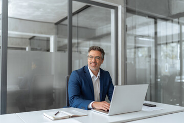Fototapeta premium Mature Latin business man ceo manager using laptop computer in modern office. Smiling senior businessman entrepreneur sitting at desk working on pc financial project, looking thinking at copy space