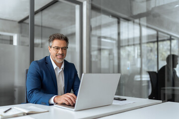 Mature Latin business man ceo manager using laptop computer in modern office. Smiling senior...