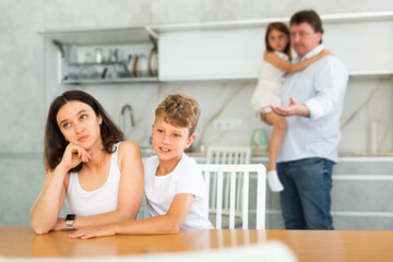 Son soothe his mother after a domestic quarrel. Father with little daughter in the background