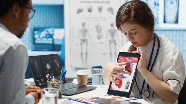 Woman specialist explaining heart function and condition on test results, doctor patient interaction in a cabinet. Physician cardiologist showing the cardiovascular system on tablet. Camera A.