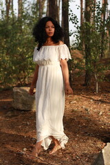 Naklejka premium Beautiful young brown haired curly woman in white dress walking in the forest