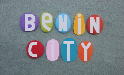 Benin City, city situated in southern Nigeria, souvenir of logo composed with multi colored hand painted stone letters over green sand