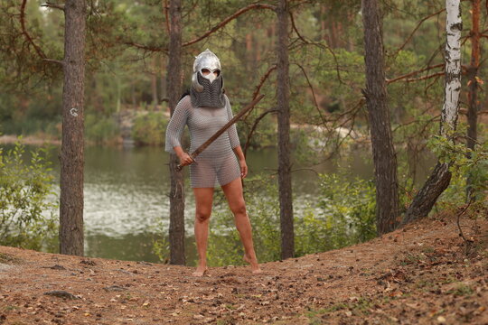 Young slender woman in chainmail and helmet holding big sword as a medieval knight standing in the forest full length