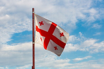 Flag of Georgia waving on flagpole on cloudy sky background