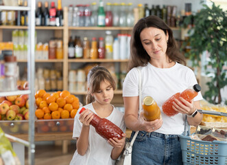 Girl and mother looking at juice in store. Market visitors choose consider bottle fruit drink. Mom...
