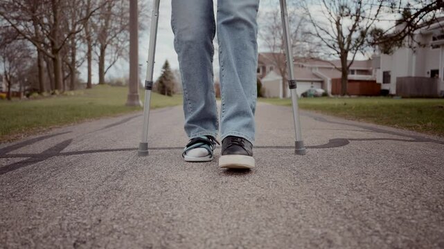 Close-up shot of a woman's legs as she walks with crutches, wearing a medical orthopedic walking boot provided in the emergency room. Footage at 60 fps
