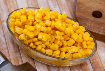 Tasty boiled sweet corn grains in bowl on wooden table