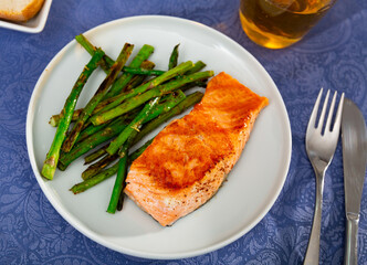 Roasted salmon steak and green asparagus served on plate.