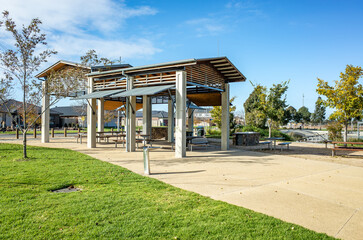 A modern outdoor pavilion in a public park, featuring picnic tables and seating areas beneath its shelter. A public recreational space in Australian neighborhood for community gatherings.