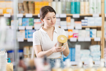 Thoughtful young woman choosing baby formula in pharmacy, reading label on container and examining...