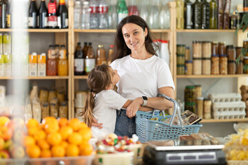 Happy and positive mother and daughter are standing in grocery store near shelves with drinks....