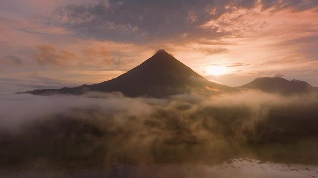 Experience the stunning sunrise at Laguna de Arenal with Volcan Arenal, showcasing Costa Ricas misty forests and serene landscapes, inviting you to explore this magical destination