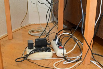 Tangled cables on the parquet floor. Overloaded electrical boards on the wooden floor. Electrical cables in disorder.