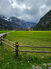 Panorama of a wooden fence, green field in a valley between high mountains with rainy clouds above