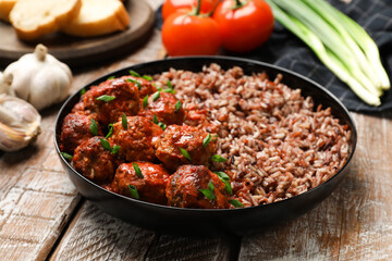 Tasty meatballs with sauce, brown rice and products on wooden table, closeup