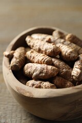 Raw turmeric roots in bowl on wooden table, closeup