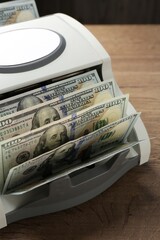 Money counter machine with dollar banknotes on wooden table, closeup